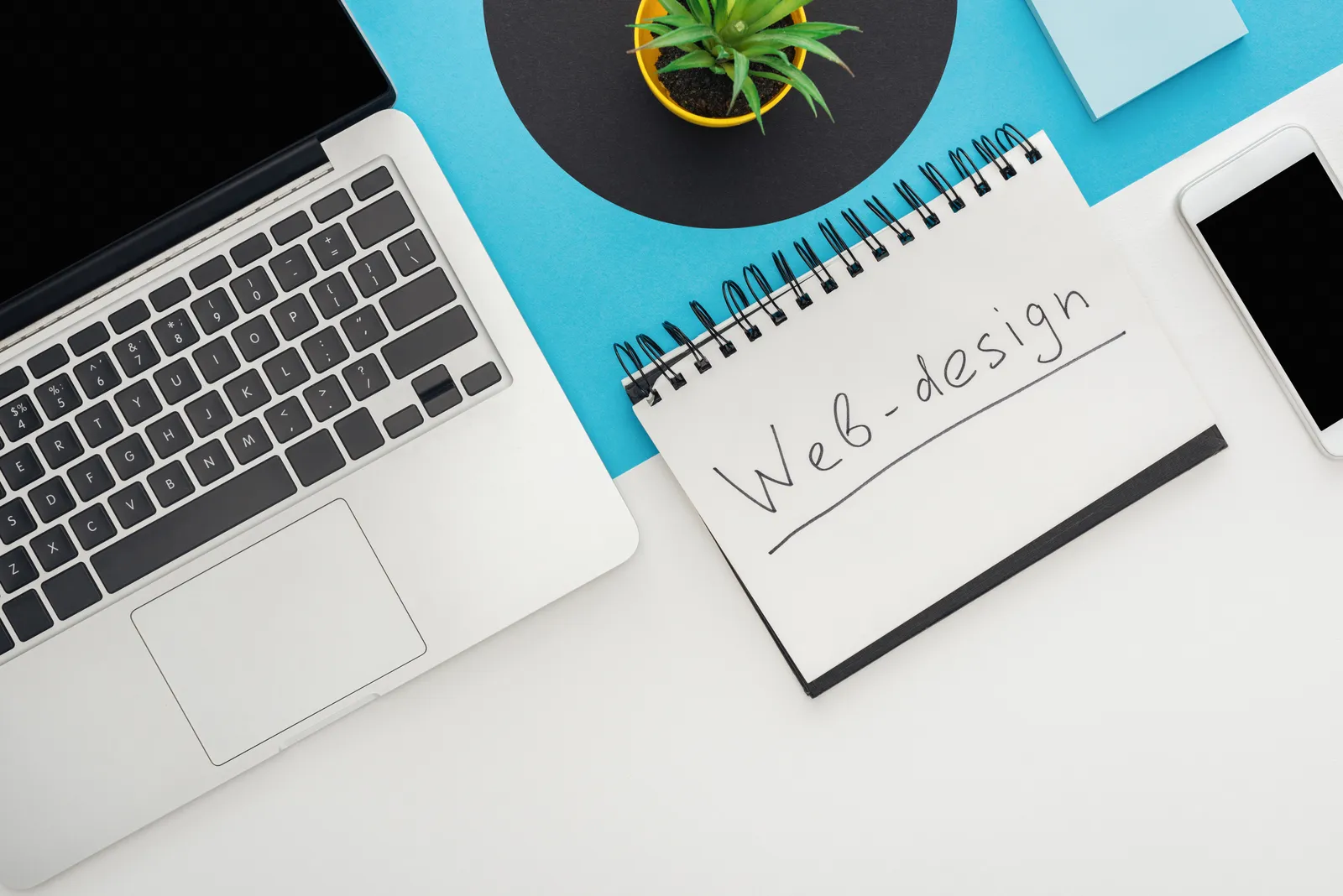 Flat lay of a laptop, notepad, phone and plant on a desk, used as a placeholder image for an article about auditing Google Ads spend